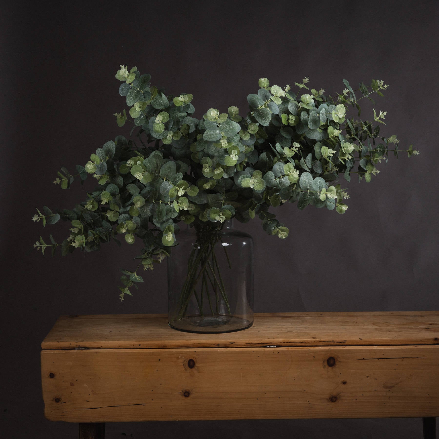 Faux eucalyptus stems styled in a clear glass vase against a neutral wall