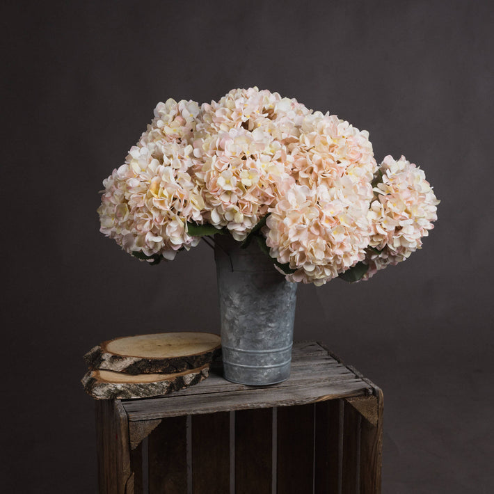 Group of faux white hydrangea stems styled in ceramic vase against neutral background