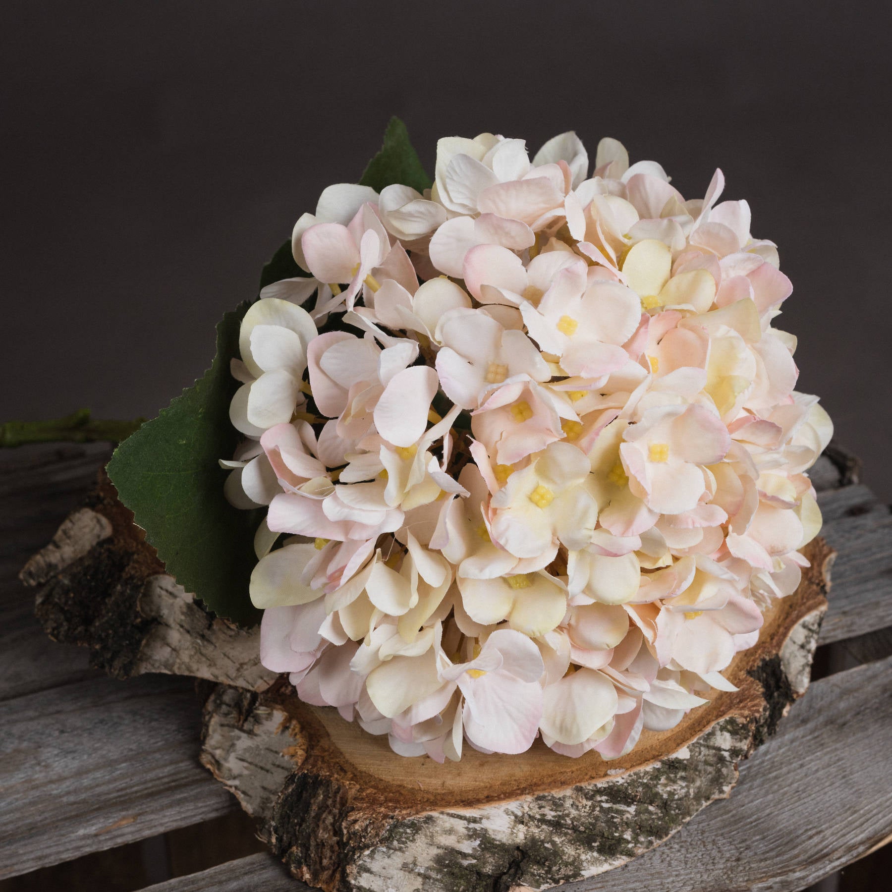 Lifestyle setting with faux hydrangea stems styled in interior corner with light decor