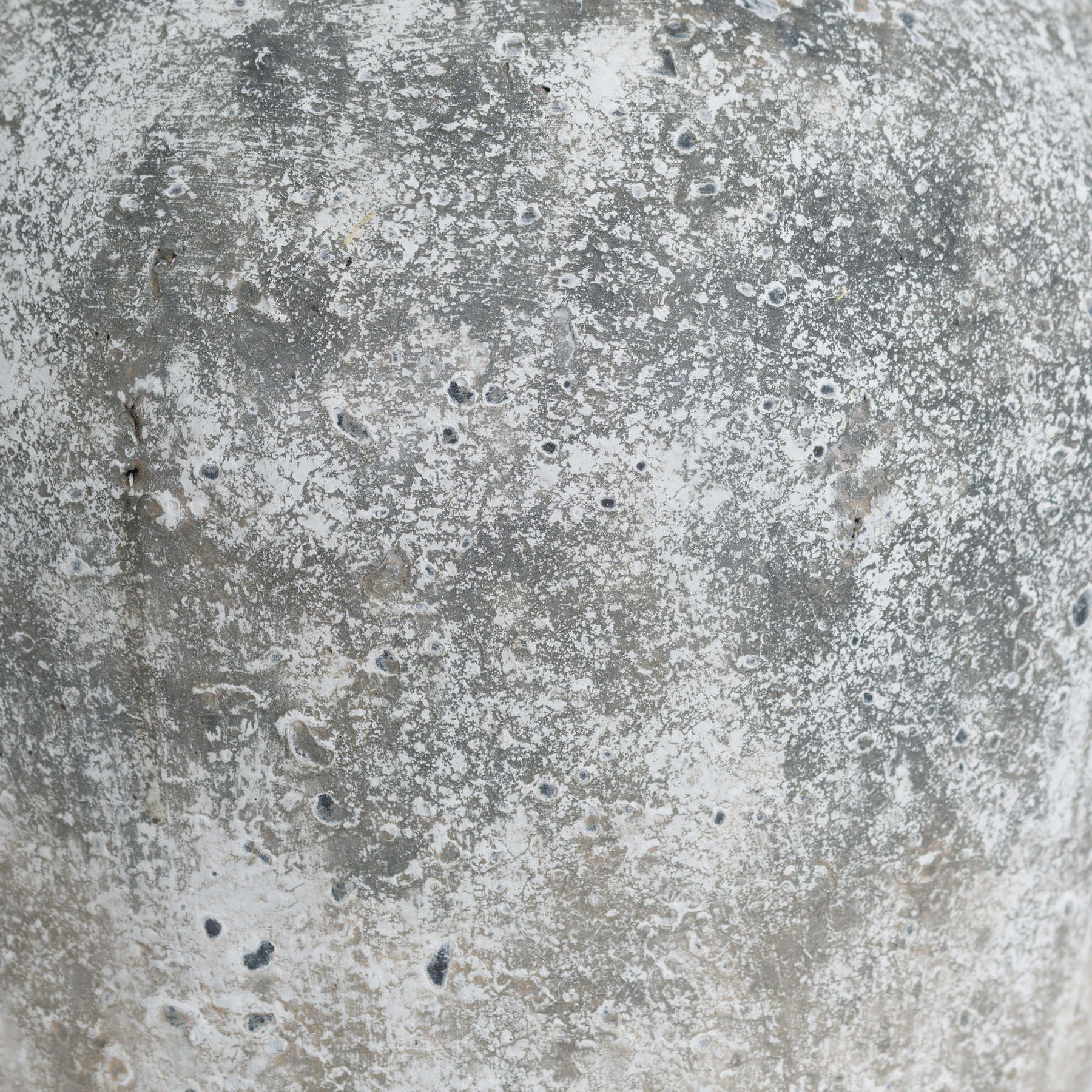 Close-up of mottled, pitted aged-stone patina on grey ceramic vase.