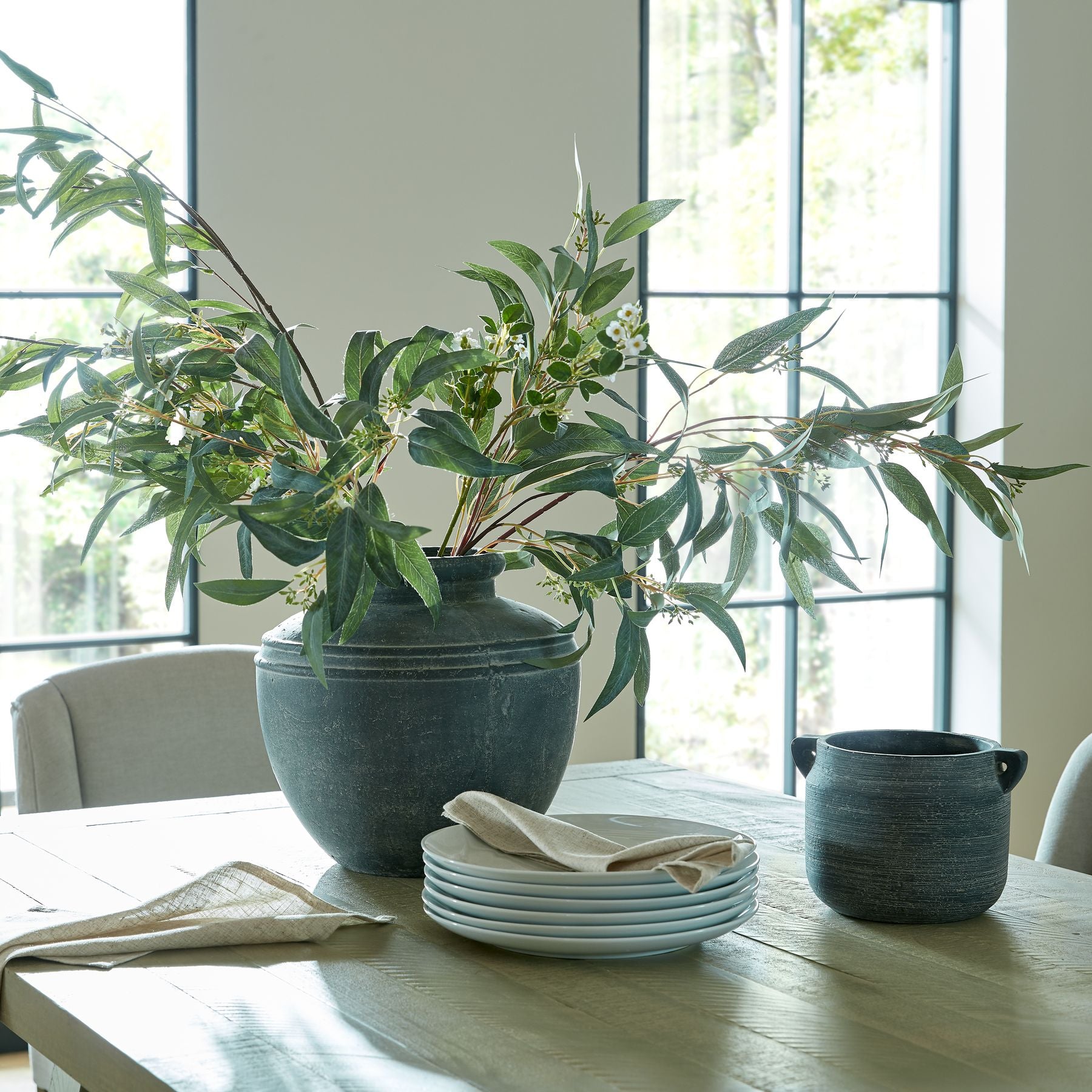 Seeded Eucalyptus Faux Spray positioned in a tall urn in a soft-brutalist living space, accentuating architectural height and sculptural form.
