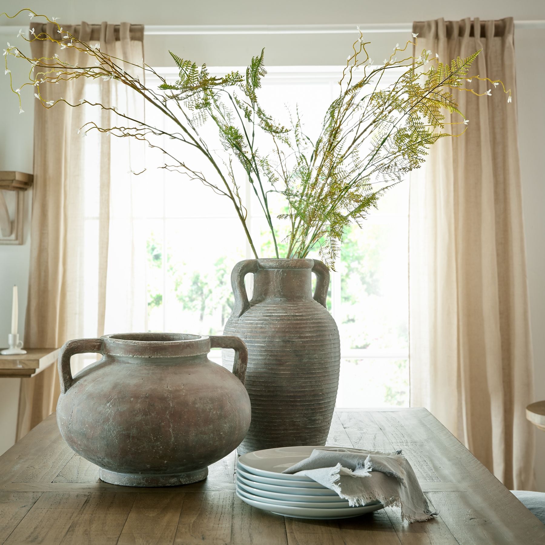 Signature Curated Dining Table Styling Kit banner featuring textured clay amphora and round terracotta vases filled with faux greenery alongside artisanal dinnerware in a minimalist brutalist‑Scandi interior by Christie’s Interior