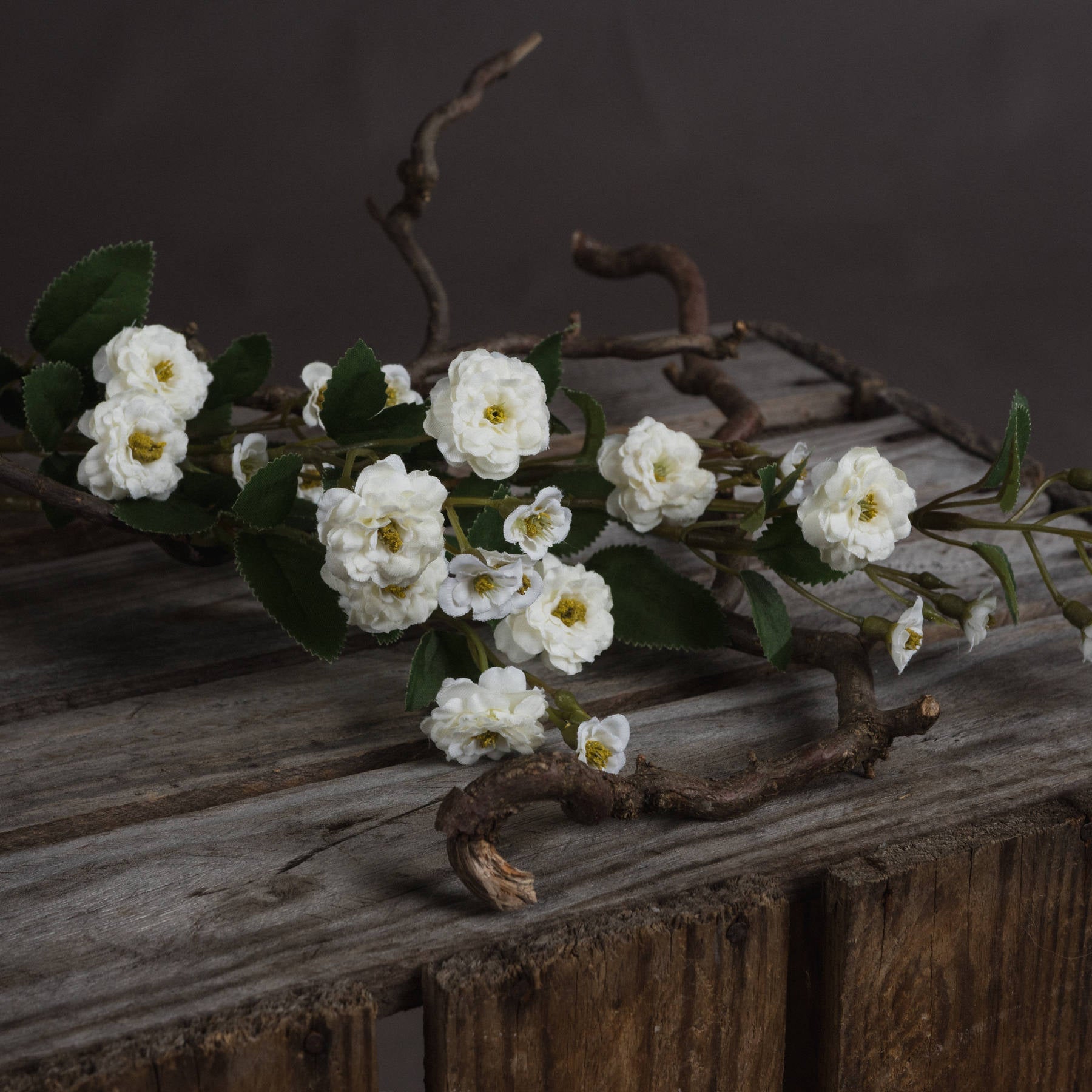 Single stem of White Wild Meadow Rose Faux Spray laid horizontally on weathered timber, highlighting realistic petal texture.