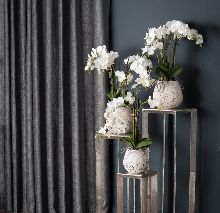 Close-up of faux Phalaenopsis orchid bloom with tonal detailing and raw ceramic pot surface texture