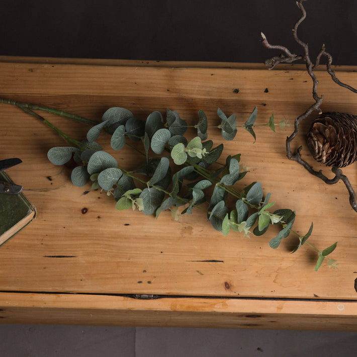 Faux eucalyptus stems laid flat on a white surface in bundle arrangement