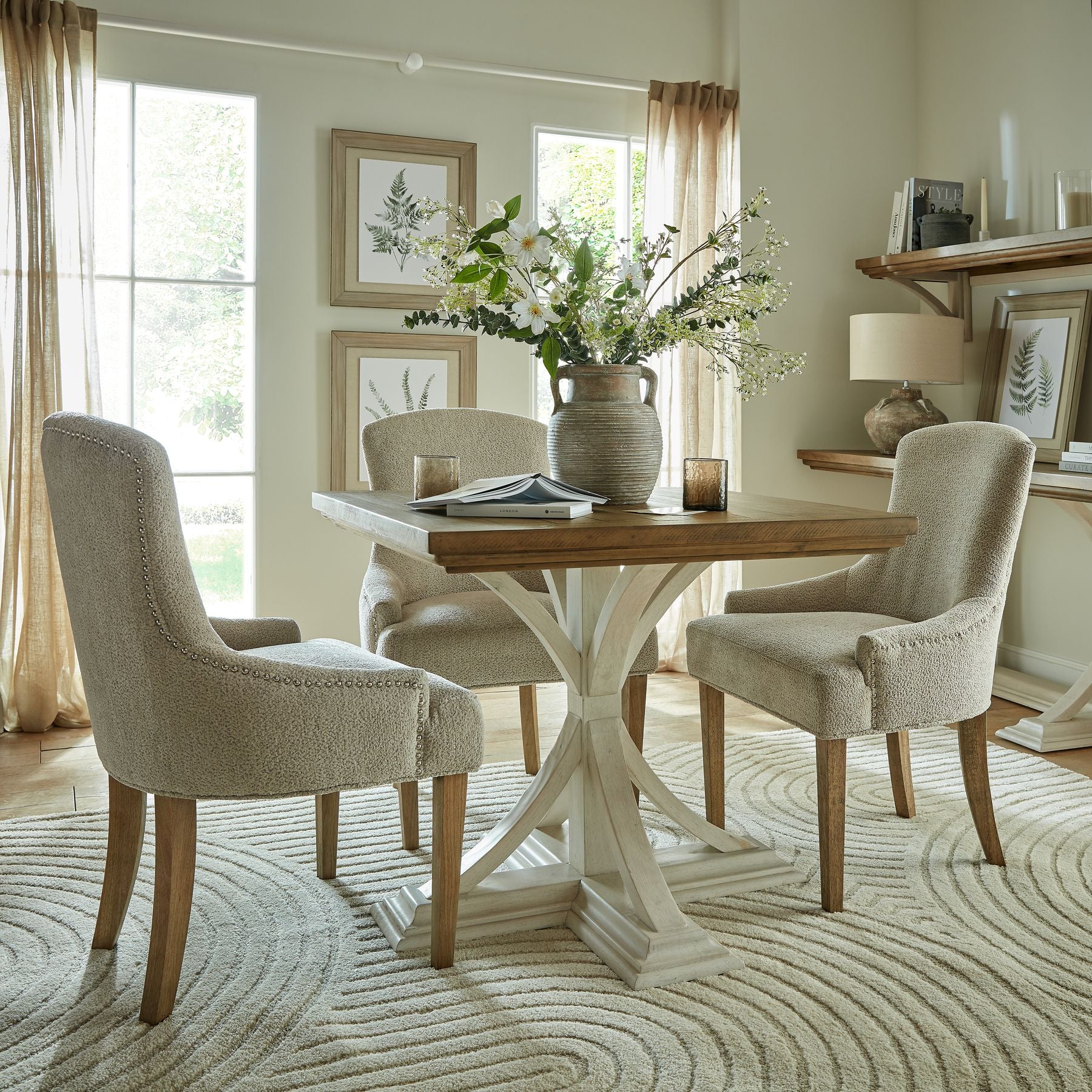 Dining room with a wooden table and chairs, decorated with flowers and books. Close-up of the clay brown stoneware surface with weathered matte glaze on the Lowther Amphora Vase.