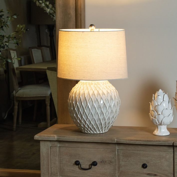 Lifestyle scene of lattice ceramic lamp styled on wooden console with neutral backdrop