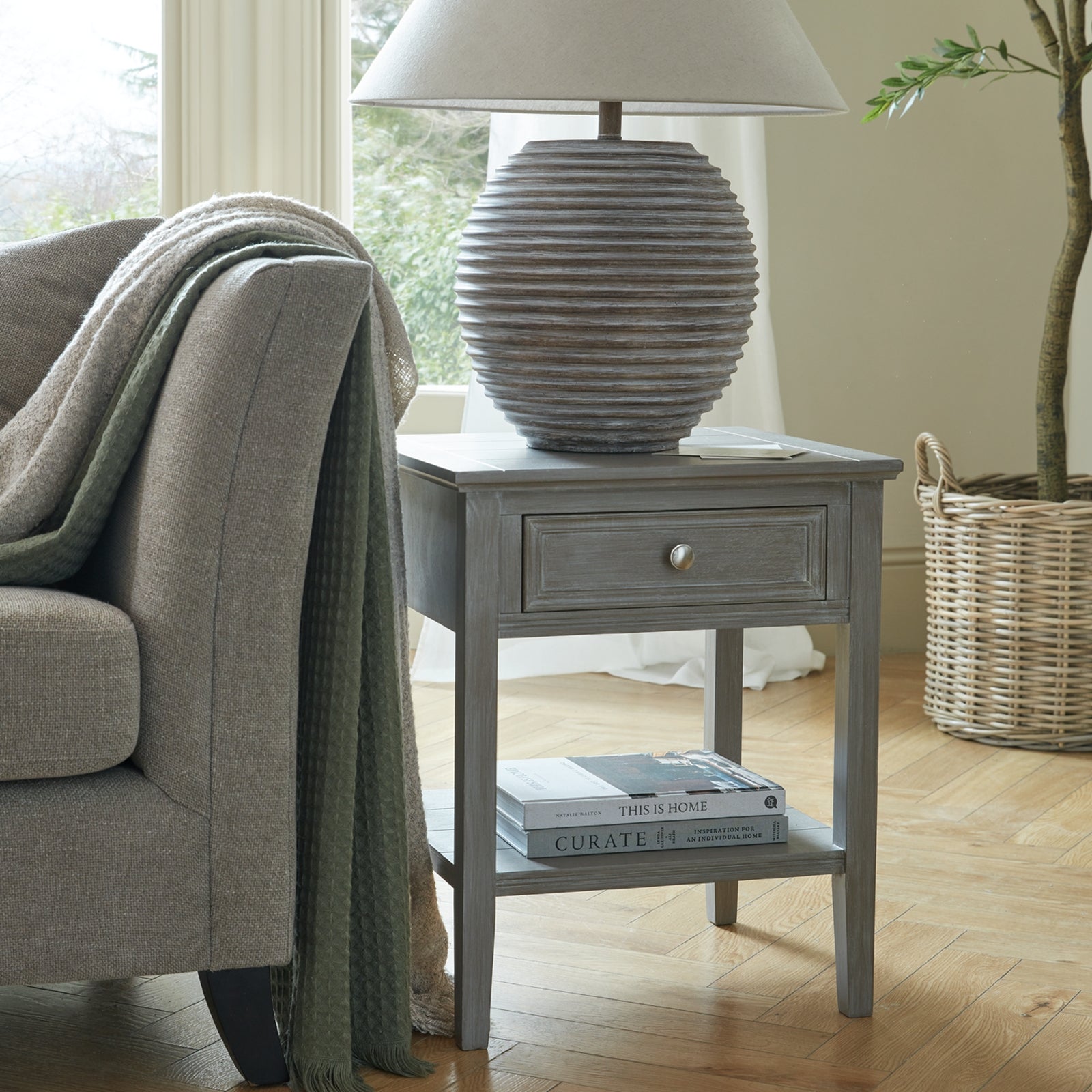 Lifestyle scene of ribbed stone ceramic lamp styled on wooden console against neutral wall
