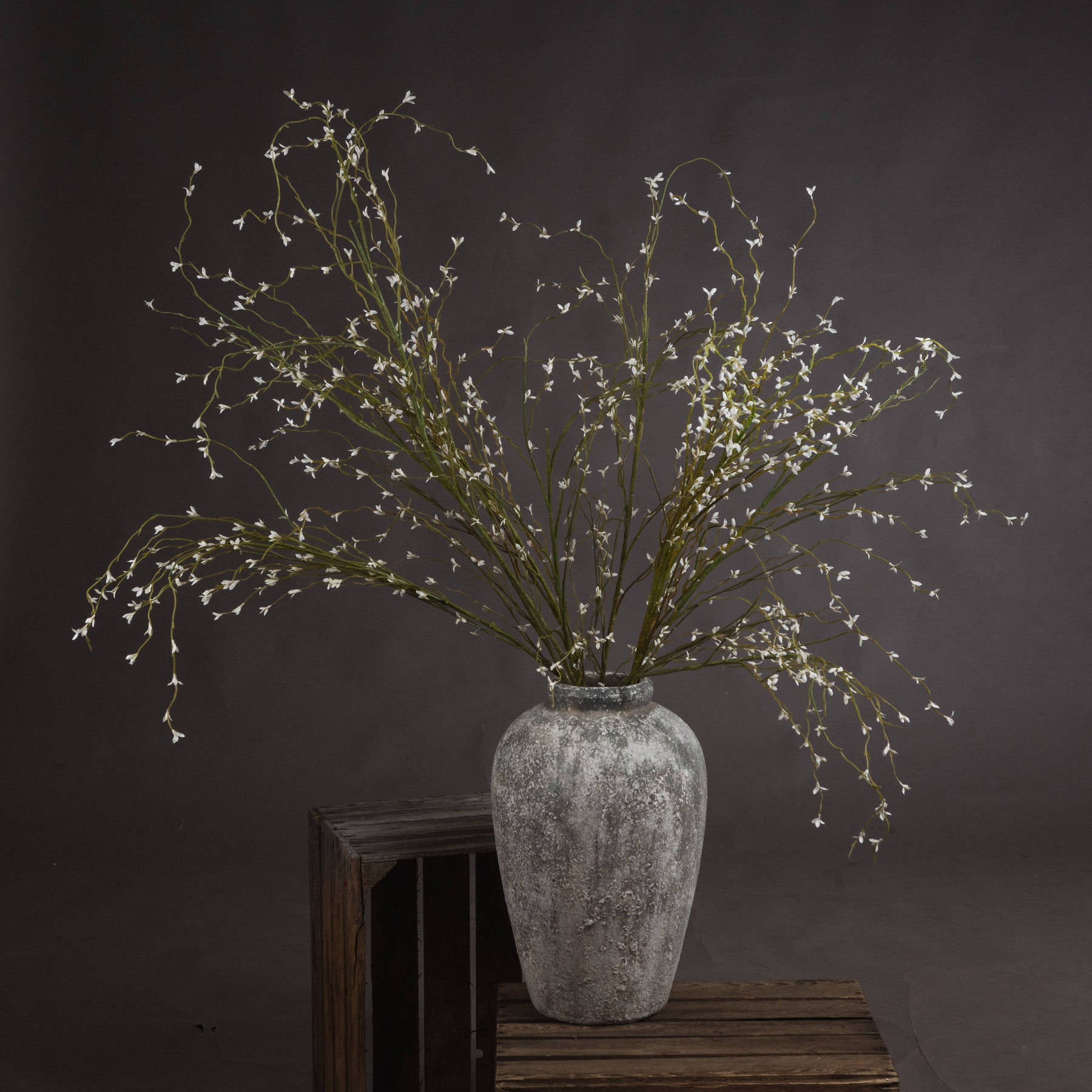 Tall white willow faux spray arranged in floor-standing ceramic vase with architectural composition